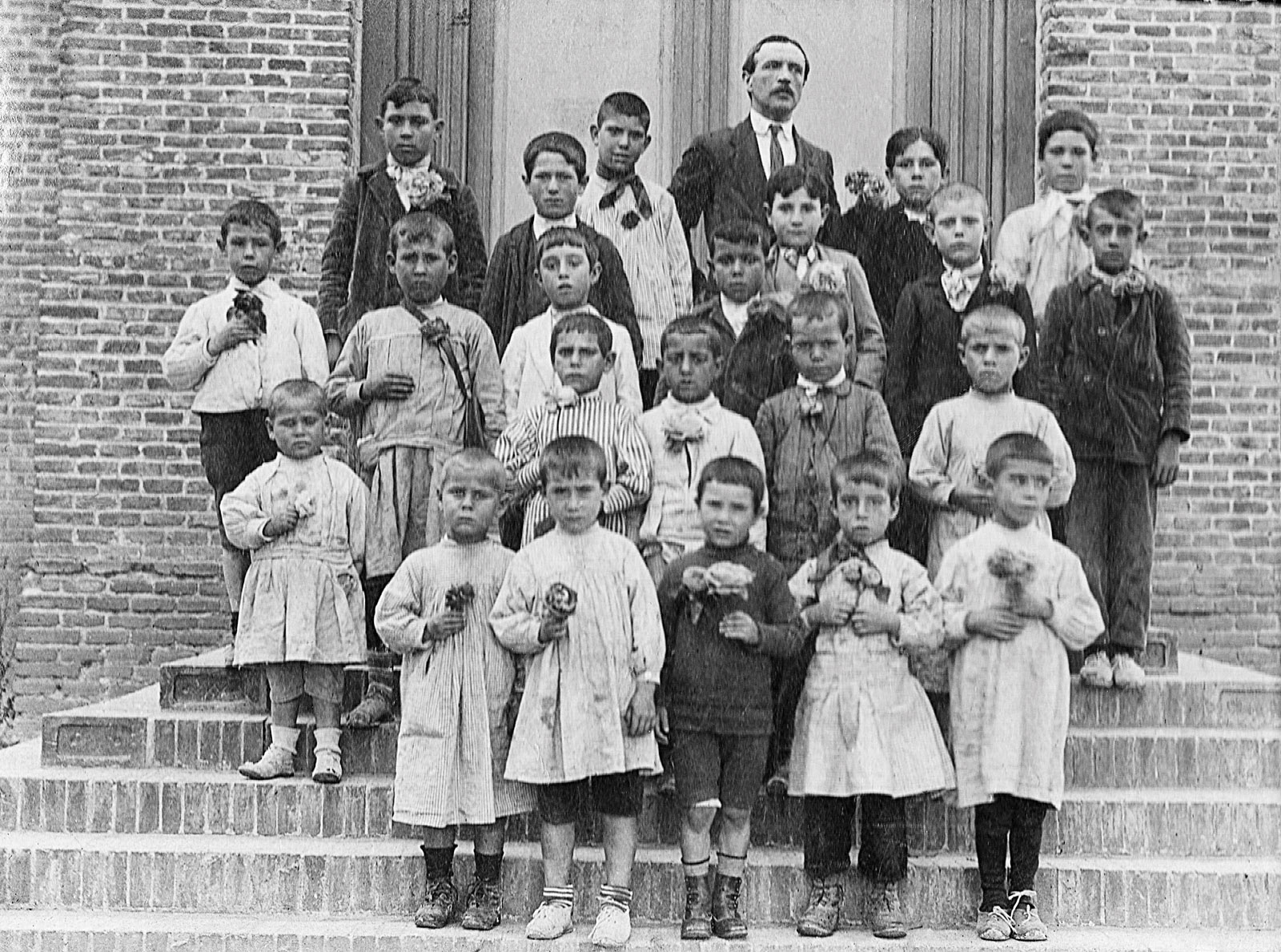 Grupo escolar con su maestro posando en la escuela pública y portando flores en la primera década del siglo XX.